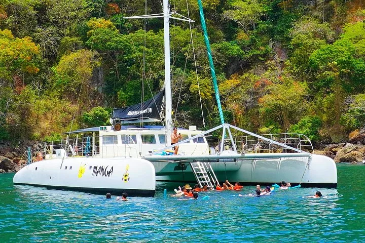 People swimming in the water next to a large anchored catamaran